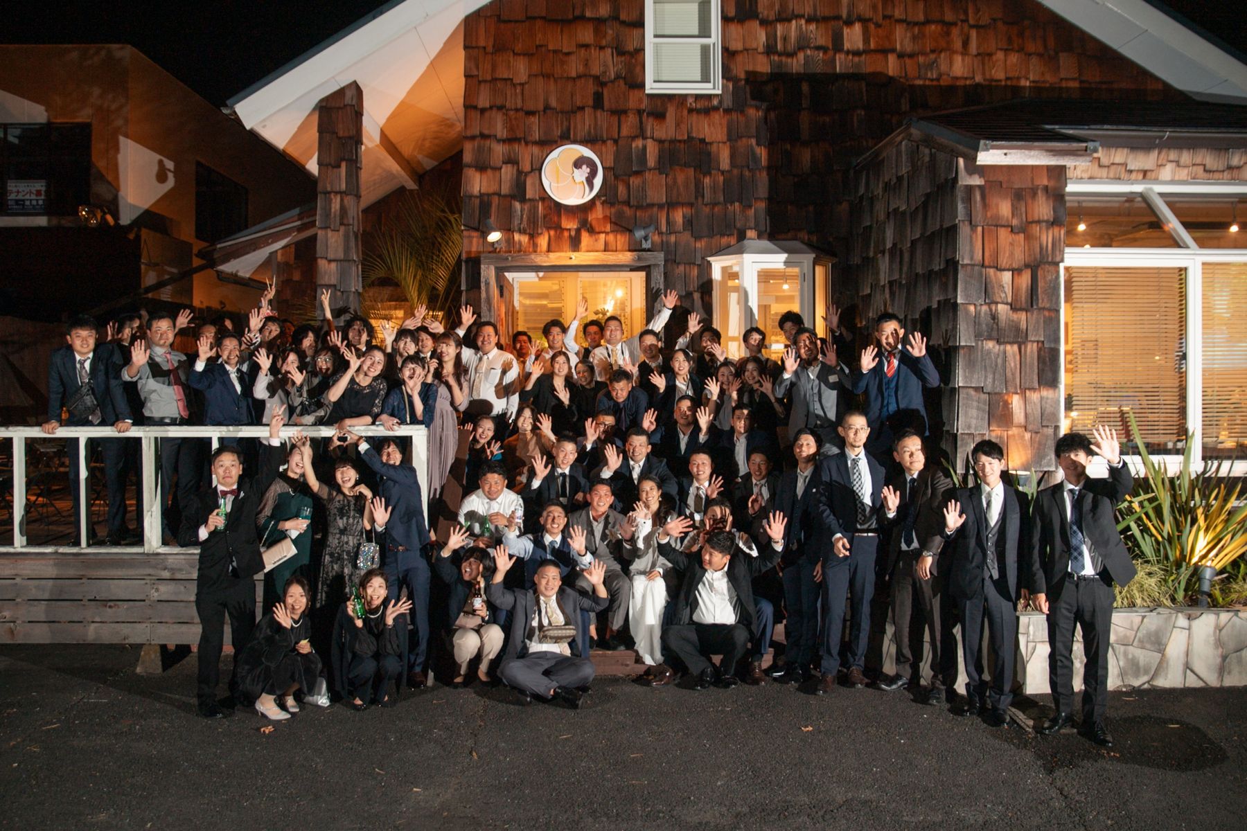 夜の外観の前で手を振るゲストたちの集合写真